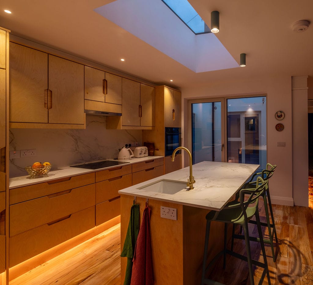 Kitchen with warm under-cabinet light and rooflight in a 1950s terrace house