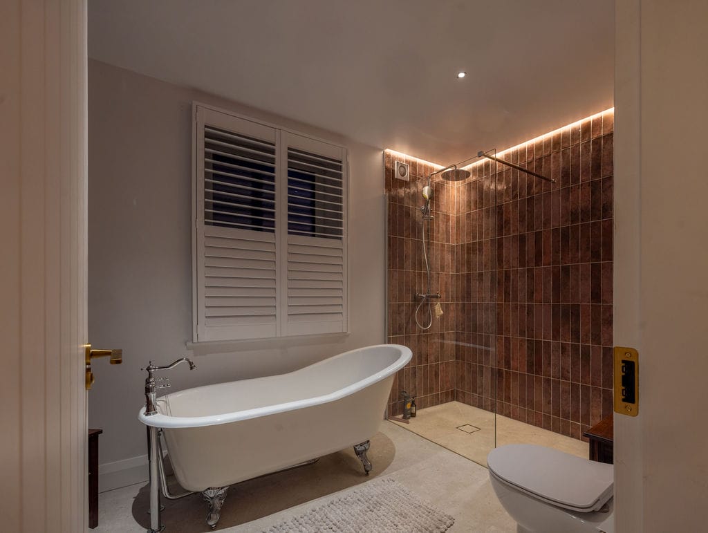 Bathroom with freestanding bath and warm wall light in a 1950s terrace house