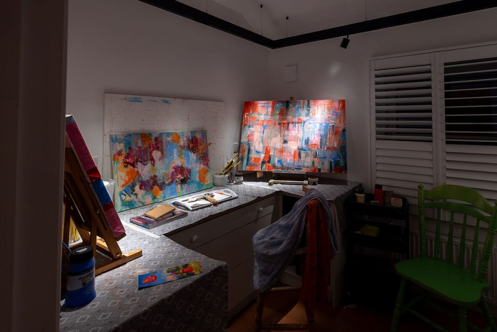 Artist’s desk and paintings in warm light in a 1950s terrace house