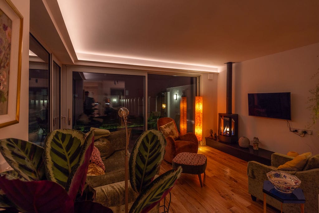 Living room with warm cove lighting and a wood stove in a 1950s terrace house, Kilkenny